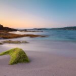Spiaggia sarda all'alba, con acque brillanti e sabbia dorata che riflette la luce del sole.
