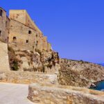 Paesino siciliano con case di pietra e vista panoramica sul mare cristallino.