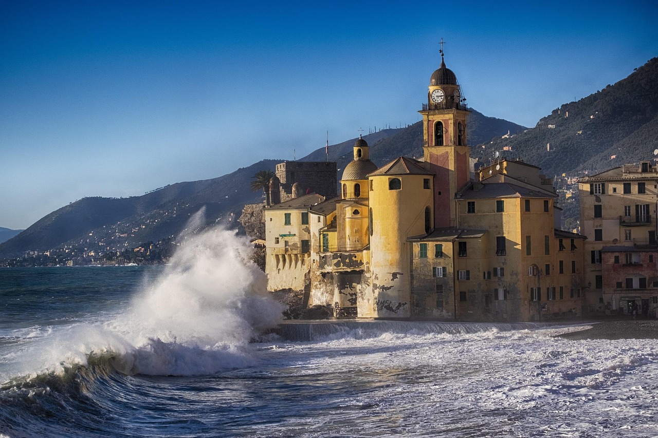 Borgo ligure con case colorate affacciate sul mare, cielo azzurro e barche ormeggiate nel porto.