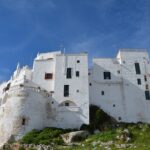 Trulli bianchi nel villaggio pugliese, circondati da natura e vista sulle spiagge nascoste.
