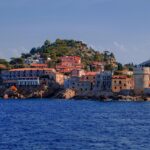 Panorama mozzafiato di un paese sardo con case colorate e mare cristallino, simile a un set cinematografico.
