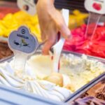 Gelato artigianale servito in un cono, con vista su una piazza italiana affollata di turisti.