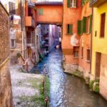 Vista panoramica di Bassano del Grappa con il ponte degli Alpini e un bicchiere di spritz in primo piano.